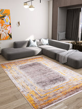 A modern living room features a gray sectional sofa, two light blue pillows, a gray blanket, a colorful abstract painting, and the Subtle Elegance - Washable Rug - JR1174 (Custom Size) in orange, yellow, and white on warm wood flooring.