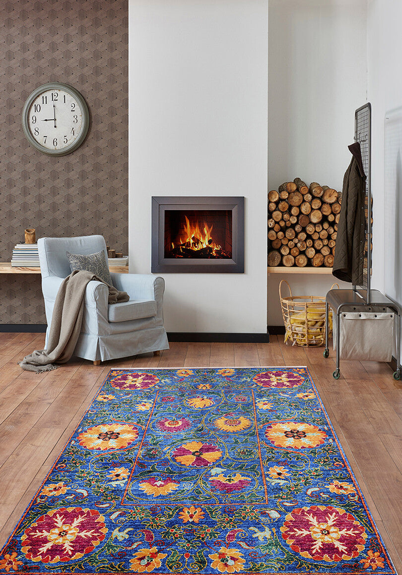 A cozy living room with the Summer Bouquet - Washable Rug - JR1358 (Custom Size), perfect for high-traffic areas, a light blue armchair with a blanket, modern fireplace, large wall clock, and wooden floors.
