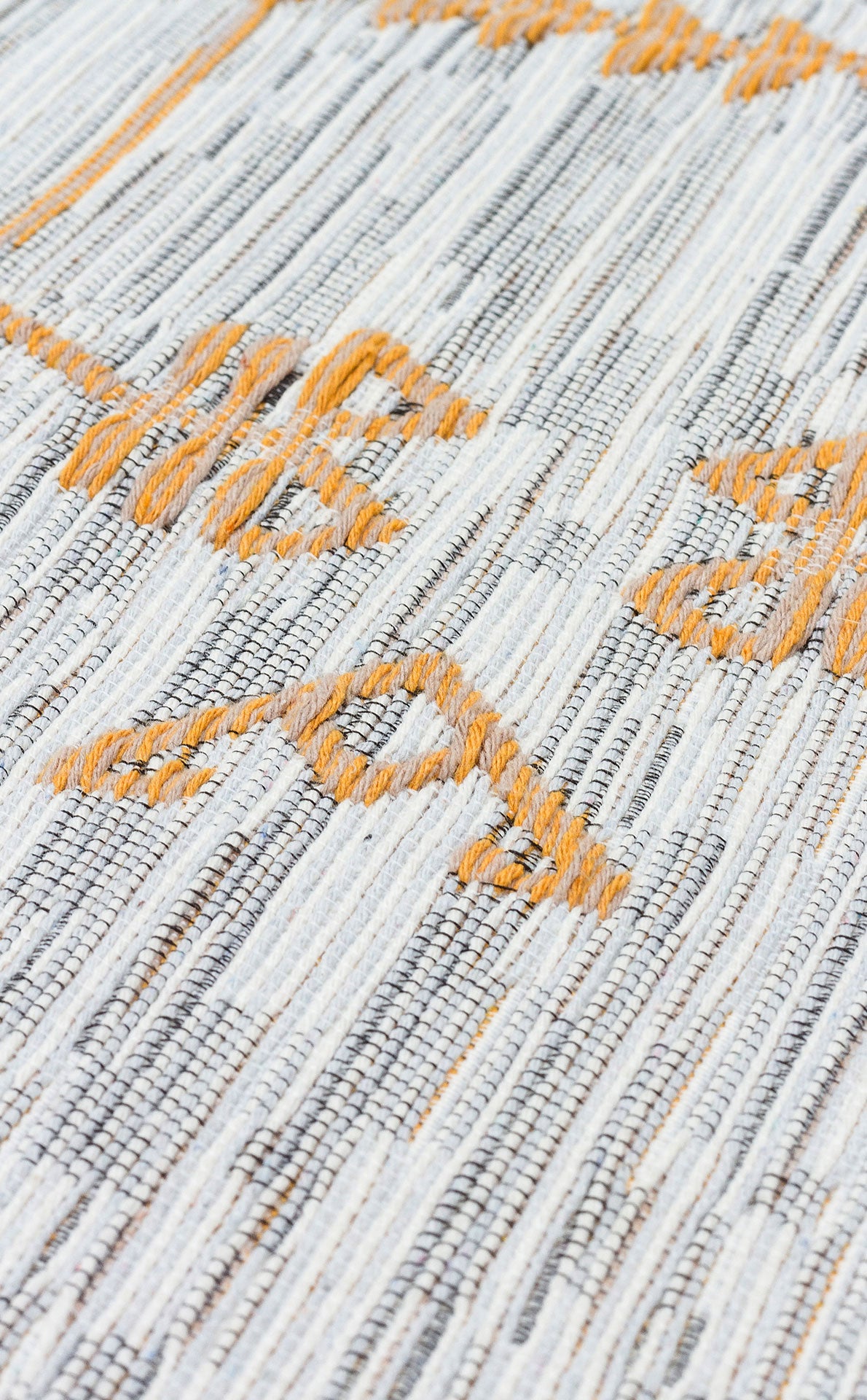 A close-up of the Sunbeam Line AR23 washable double-sided kilim reveals gray and white woven threads accented by orange geometric patterns on its textured surface.
