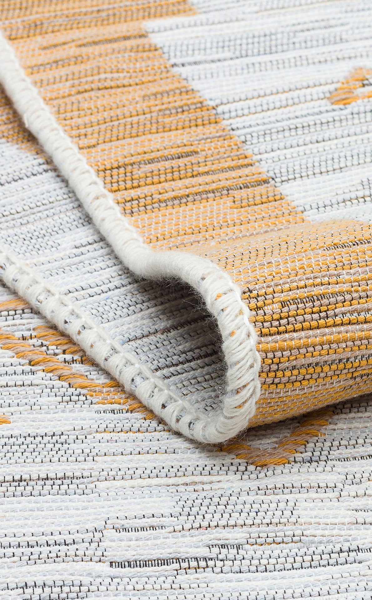 A close-up of the Sunbeam Line - Washable Double-Sided Kilims - AR23 displays its tan and white stripes, with the rug partially folded to highlight its detailed stitching and textured fabric.