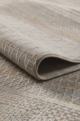 A close-up of the Sunkissed Boho Trellis Rug - M627M, rolled up to reveal its textured surface with subtle diamond and linear patterns in muted beige, gray, and taupe tones.