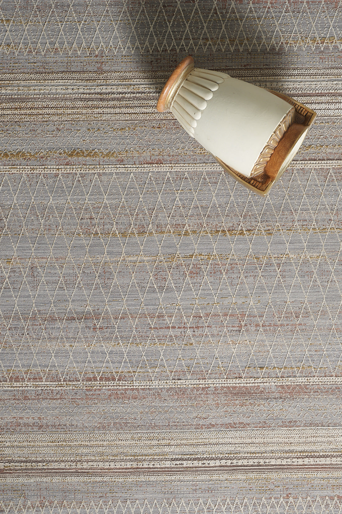 A beige and brown ceramic vase lies on its side atop the Sunkissed Boho Trellis Rug - M627M, which features a modern geometric diamond pattern in shades of gray, beige, and gold.