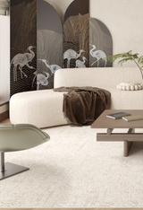 A modern living room with a curved white sofa, brown throw, light green swivel chair, wooden coffee table with books, and a crane screen—all atop the Sunset Fade - Washable Rug - JR1878 (Custom Size) for added warmth.