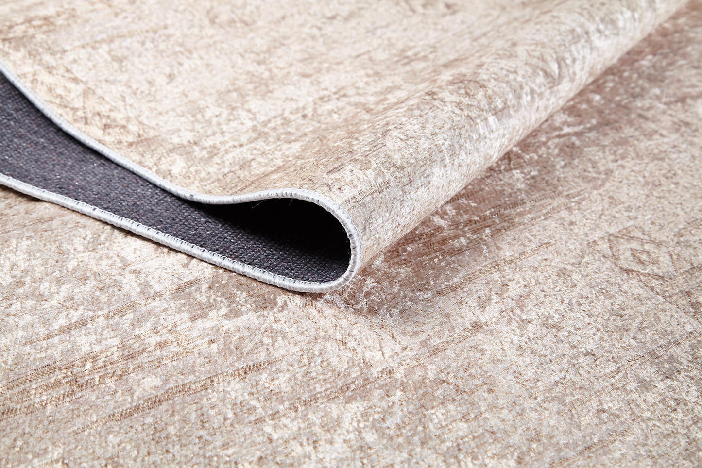 A close-up of the Sunset Fade - Washable Rug - JR1878 (Custom Size) in beige, showing its textured flat weave, subtle distressed pattern, and a flipped corner that reveals the dark, non-slip backing. This rug is fully washable.