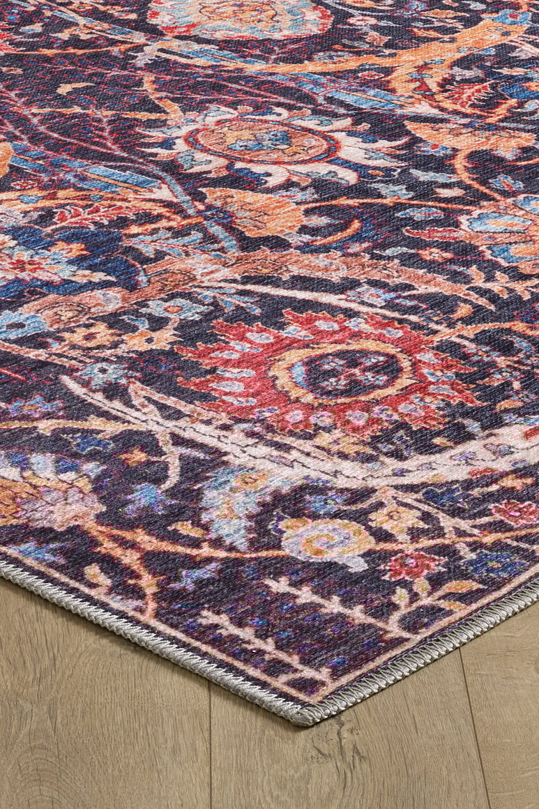 A close-up of the Sylvanor Colorful Washable Rug - LCC3017 on a light wood floor, showing its intricate red, orange, blue, and cream floral patterns, detailed border, and textured edges in a Persian-inspired design.