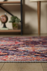 A close-up of the Sylvanor Colorful Washable Rug - LCC3017 on a wooden floor, ideal for high-traffic areas, with a potted plant, decorative clock, and wooden furniture legs in the softly blurred background.