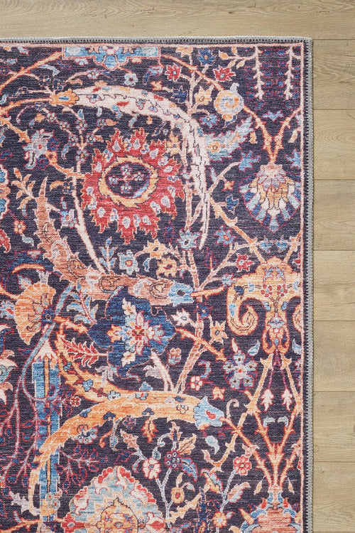 Load image 1 in gallery view. A close-up of the Sylvanor Colorful Washable Rug - LCC3017 (Custom Size) shows its intricate red, gold, blue, and ivory floral and vine pattern on a dark purple background, with just a corner visible on a light wooden floor. Perfect for high-traffic areas.