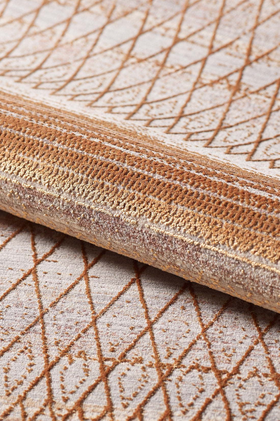 A close-up of the Tangerine Dream Trellis Rug - HRD008, a rolled-up beige machine-made rug featuring a brown geometric diamond pattern. The woven viscose polyester material and intricate design are clearly visible.