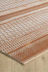 A close-up of the Tangerine Dream Trellis Rug - HRD008, a machine-made viscose polyester rug with geometric rust and cream patterns, fringed short sides, shown on a light wooden floor.
