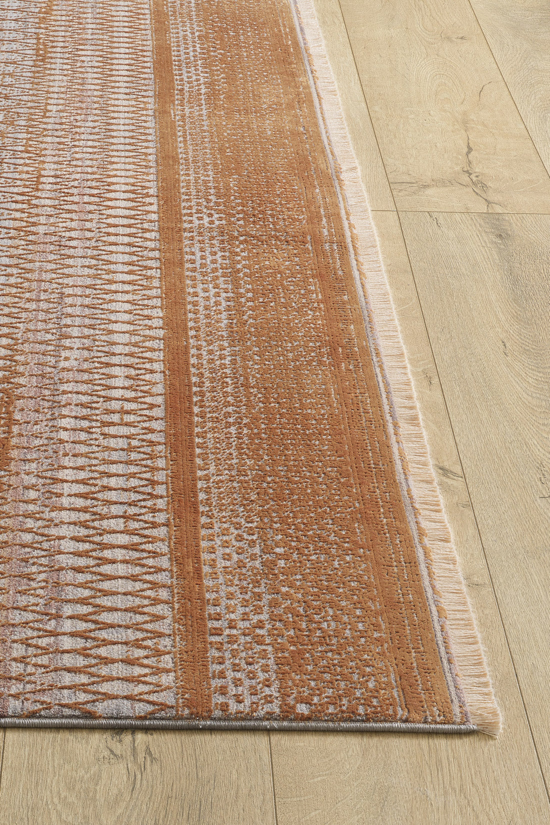 A close-up of the Tangerine Dream Trellis Rug - HRD008 shows orange and white diamond patterns with fringe edges on a light wood floor. This machine-made rug features linear motifs in varying densities for a contemporary look.