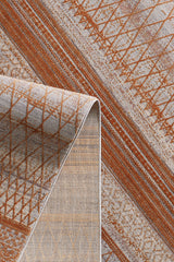 A close-up of the Tangerine Dream Trellis Rug - HRD008, folded to show its modern diamond pattern in rust orange and gray with diagonal lines and diamond shapes on a textured surface.