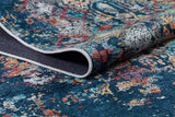 A close-up of the Tarnished Elegance - Washable Rug - JR1095 (Custom Size) in vibrant blue with teal, red, yellow, and white patterns; one corner is folded to reveal its detailed texture and dark underside—ideal for high-traffic areas.