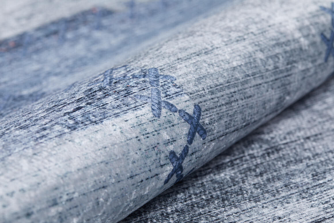 A close-up of the Tartan Twist - Washable Rug - JR31 (Custom Size) shows textured blue-gray fabric with stitched X patterns in dark blue, a rolled edge, and soft, woven look—perfect as a flat weave rug that's stylish and practical.