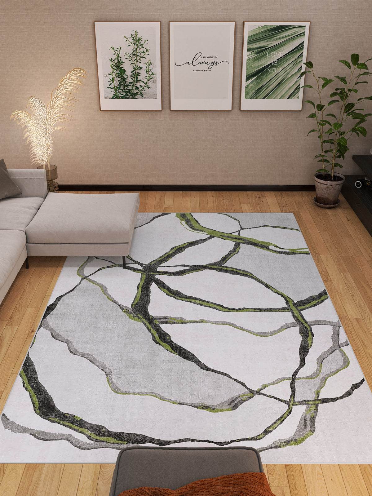 A modern living room with a light gray sectional, potted plants, wooden flooring, three botanical prints, and the Tattered Grace - Washable Rug - JRN49 featuring black and green abstract lines.
