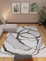 A modern living room with a light gray sectional, potted plants, wooden flooring, three botanical prints, and the Tattered Grace - Washable Rug - JRN49 featuring black and green abstract lines.