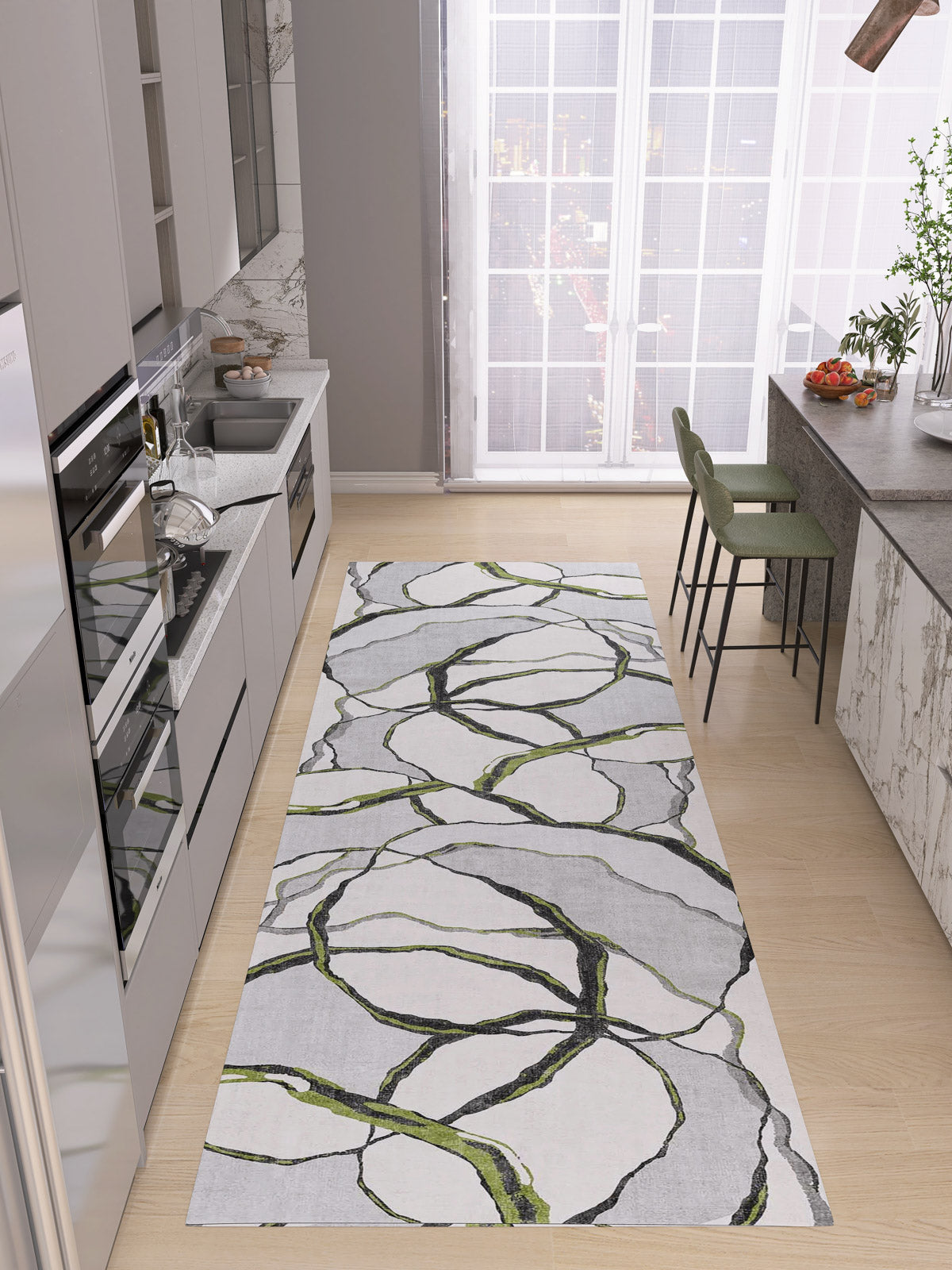 A modern kitchen with light wood floors, gray cabinetry, and a large window features the Tattered Grace - Washable Rug - JRN49 with abstract green and black lines. Two green barstools sit at the gray kitchen island.