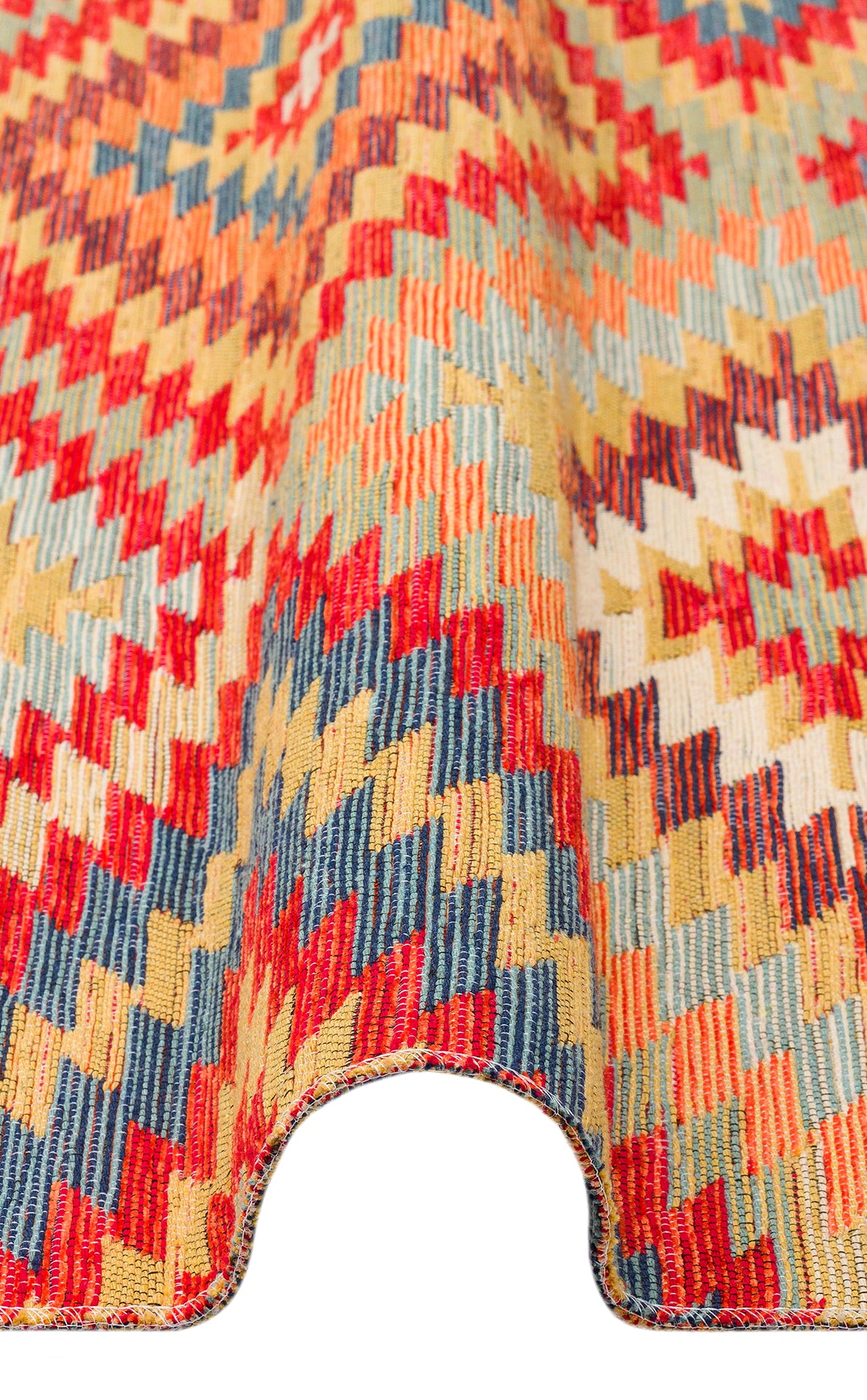 A close-up of the Terra Thread - Kilim - NMD07 textile, featuring vibrant tribal motifs and zigzag patterns in red, yellow, blue, and beige tones, draped with a soft curved fold at the bottom edge.