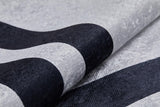Close-up of the Timeless Border - Washable Rug - JR572 (Custom Size) in gray-anthracite with bold, curved black stripes. Its soft, subtly shiny material is partially folded—durable and washable for high-traffic areas.