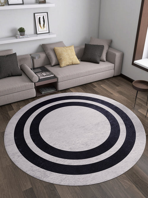 Load image 1 in gallery view. A modern living room features a beige sectional, gray and yellow cushions, wooden floor, and the Timeless Border - Washable Rug - JR572 (Custom Size) in gray-anthracite—ideal for high-traffic areas. Shelves with decor and a window are visible behind.