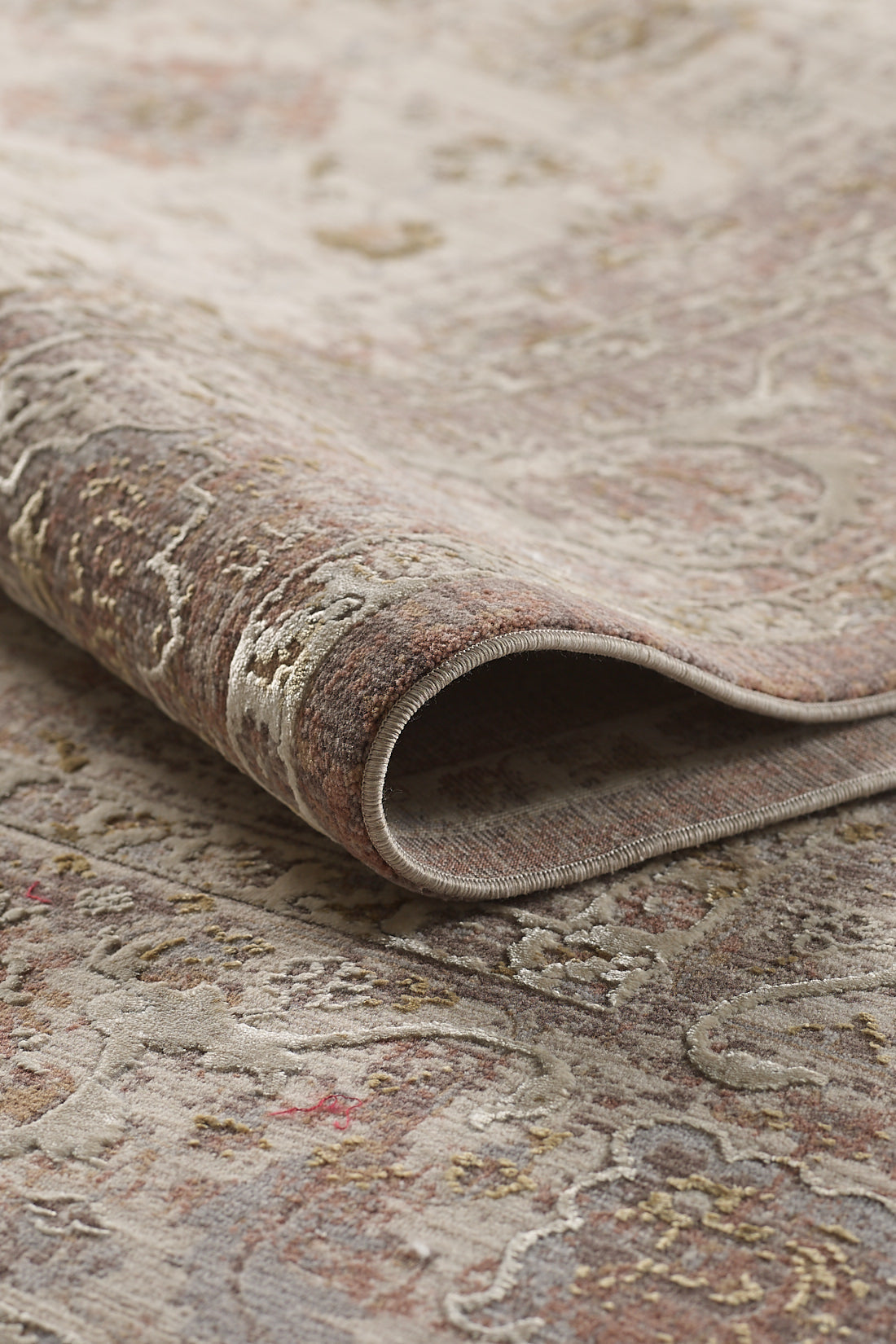 A close-up of the Timeless Petals Oushak Rug - Sand - M621N showcases its textured, weathered patterns in muted earth tones with a gentle fold along one edge and intricate design details.
