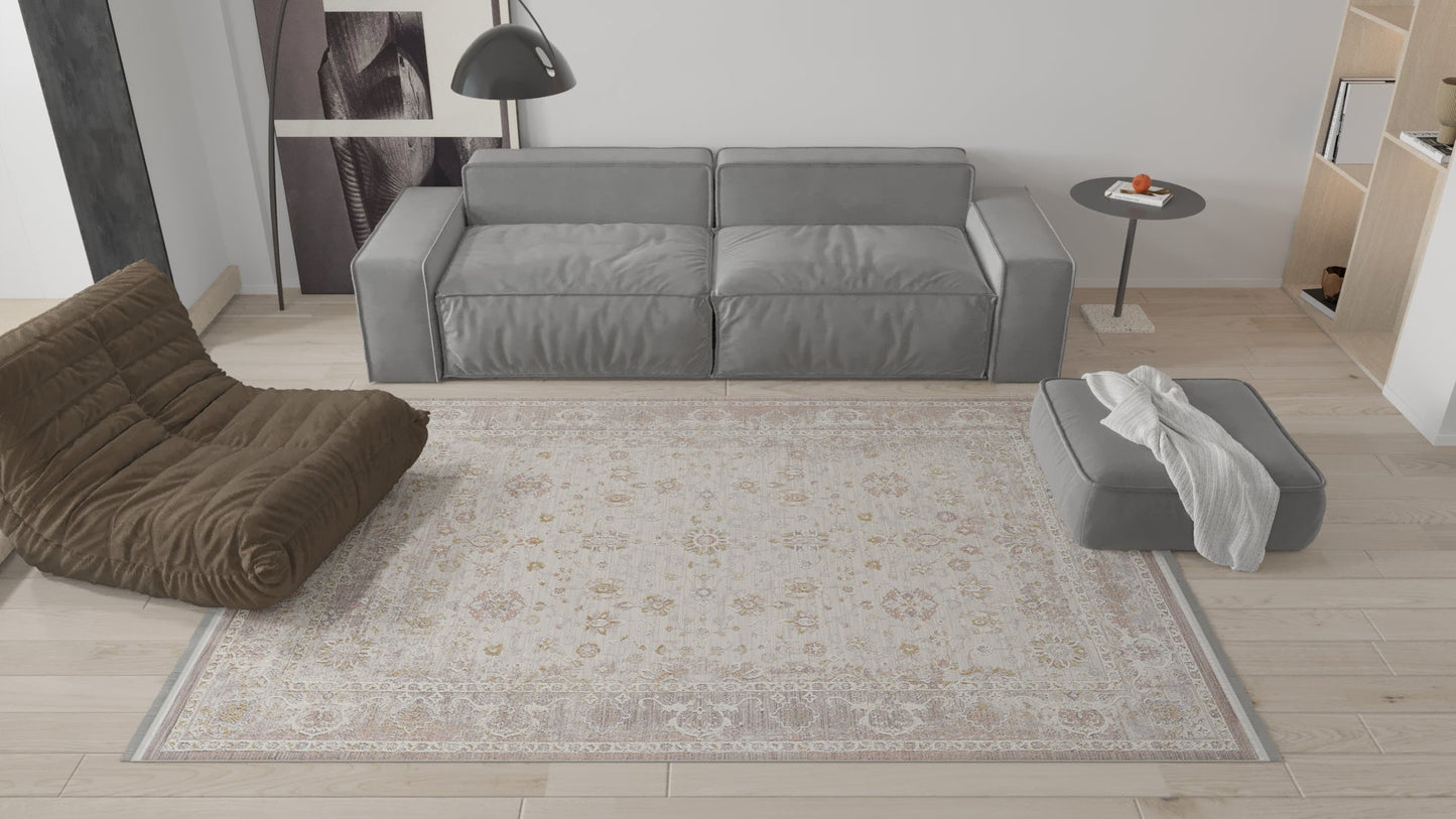 A modern living room with a gray sofa, brown lounge chair, gray ottoman with white throw, round side table, and the Timeless Petals Oushak Rug - Sand - M621N on light wood flooring. Minimalist decor in neutral tones.