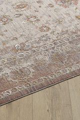 The Timeless Petals Oushak Rug - Sand - M621N features floral designs in muted beige, pink, and gray on a viscose-polyester blend. This machine-made rug has a distressed, vintage look and is displayed on a light wood floor.