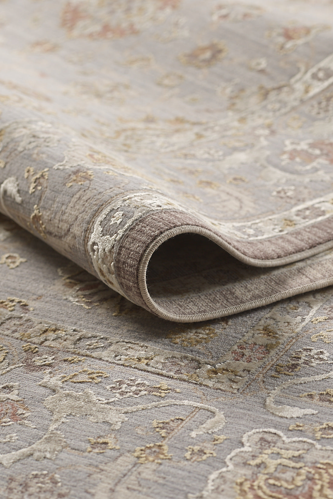 A close-up of the Timeless Petals Oushak Rug - Silver - M621O, showcasing its folded, patterned surface with traditional motifs in muted beige, gray, and gold tones. The detailed weave highlights its expert craftsmanship.