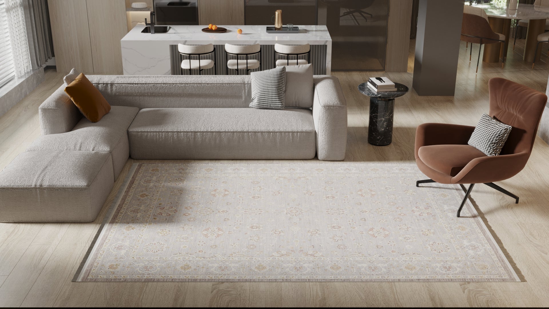 A modern living room features a light gray sectional, brown lounge chair, marble side table, kitchen island with barstools in the background, and is anchored by the Timeless Petals Oushak Rug - Silver - M621O. Natural light fills the space.