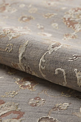 A close-up of the Timeless Petals Oushak Rug - Silver (M621O) shows its textured beige and light brown pattern on a muted gray background, with a soft surface and slightly raised areas for added depth.