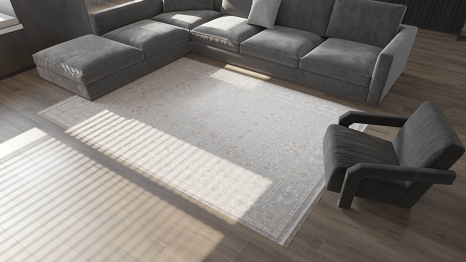 A modern living room features a gray sectional, matching armchair, and the Timeless Petals Oushak Rug - Silver - M621O on wooden floors. Sunlight filters through blinds, casting gentle shadows across the elegant space.