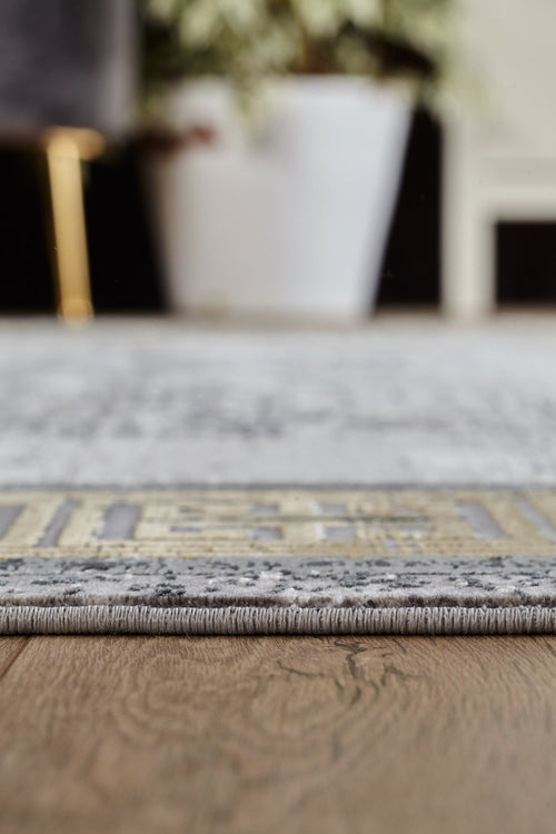 Load image 1 in gallery view. Close-up of the Timeless Remix Bordered Rug - Beige - MT187 on a wooden floor, highlighting its detailed edge and texture. A blurred white plant pot and furniture in the background enhance the rug’s stylish machine-made design.