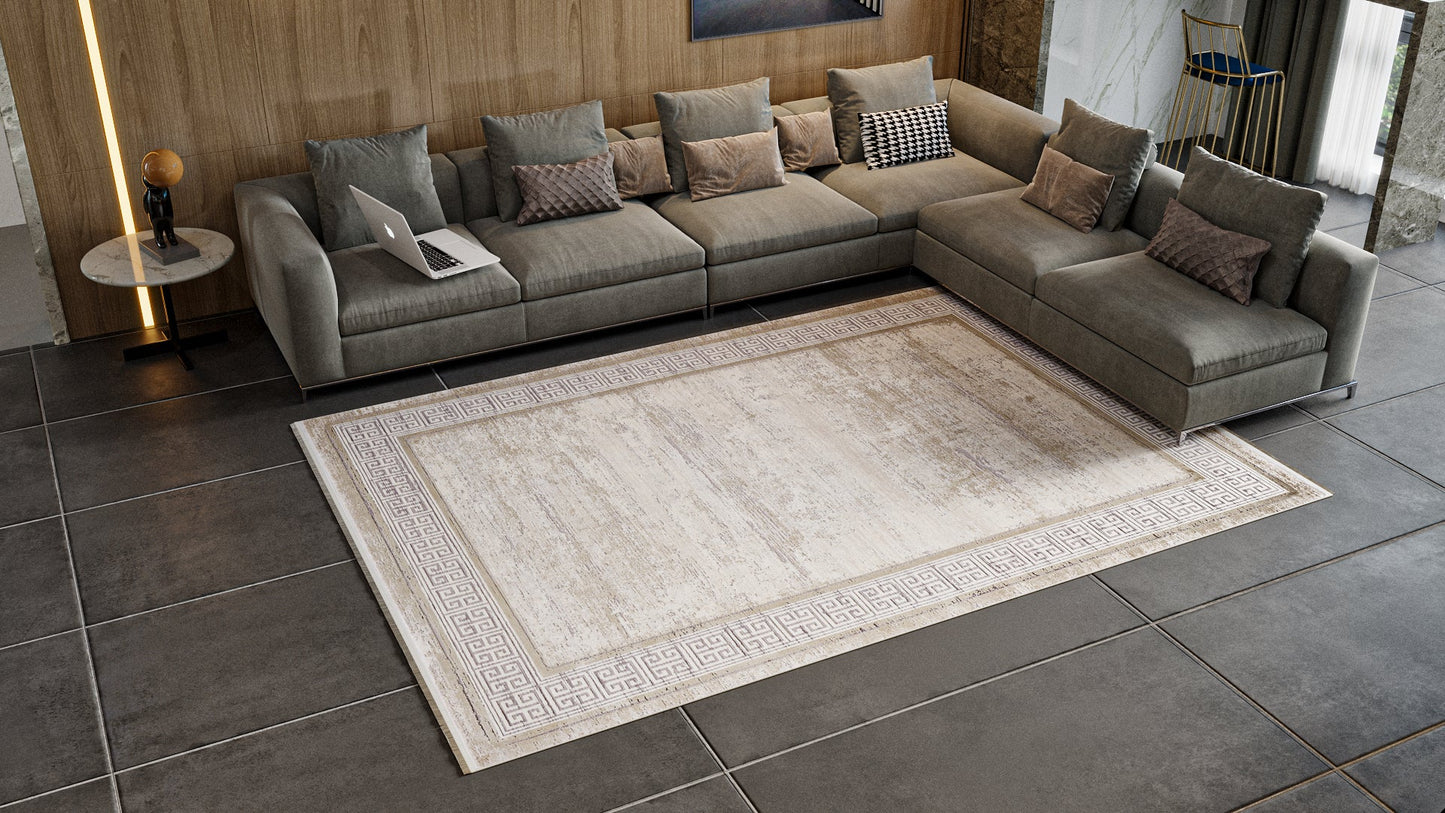 A modern living room with a large gray sectional sofa, patterned pillows, and the Timeless Remix Bordered Rug in Cream (MT189). A round side table with a lamp and a laptop on the sofa complete the look amid tile floors and wood-paneled walls.