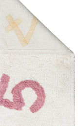 A close-up of the Tiny Joy - Washable Shaggy - CBN02 rug, featuring a white textured surface, pink curved design, and yellow X-shaped pattern on the folded corner—perfect as a playful kids room rug.