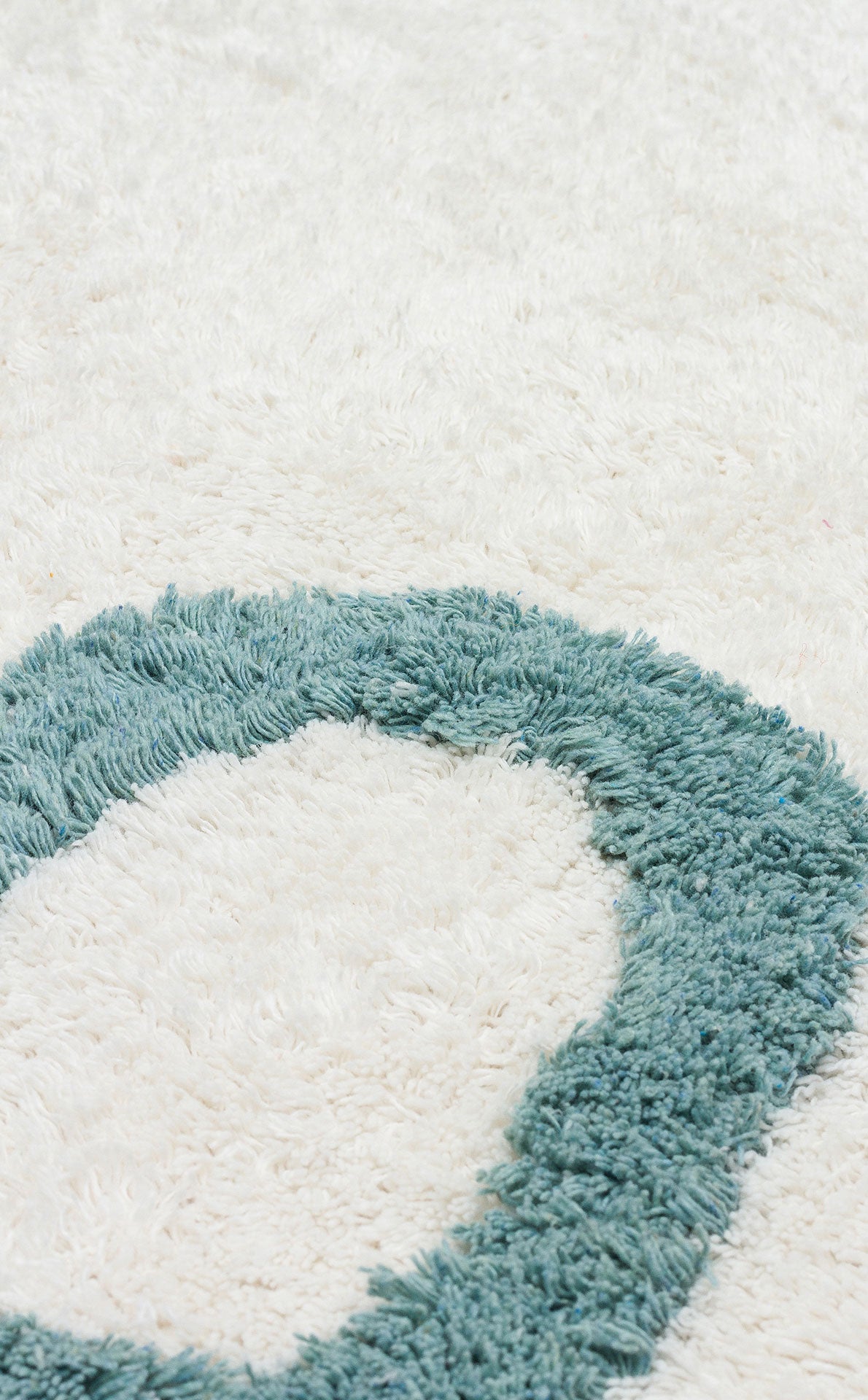Close-up of the Tiny Joy - Washable Shaggy - CBN02, a fluffy white rug with a textured teal oval pattern. Its soft, plush surface is perfect for adding comfort and style to any kids room rug collection.