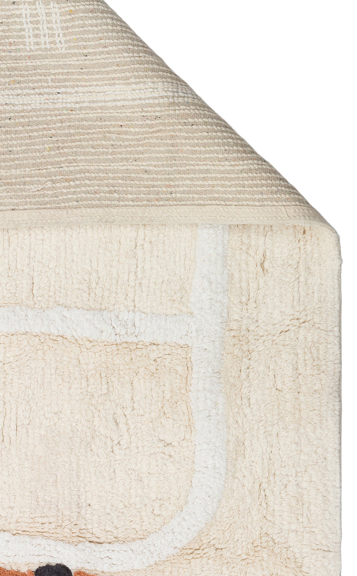 A close-up of the Tiny Voyage - Washable Shaggy - CBN09 playroom rug in beige cotton, with a folded corner showing its woven underside. Its visible side displays white and black lines in the design.