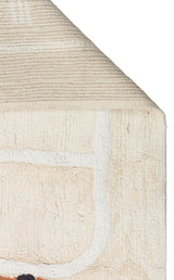 A close-up of the Tiny Voyage - Washable Shaggy - CBN09 playroom rug in beige cotton, with a folded corner showing its woven underside. Its visible side displays white and black lines in the design.