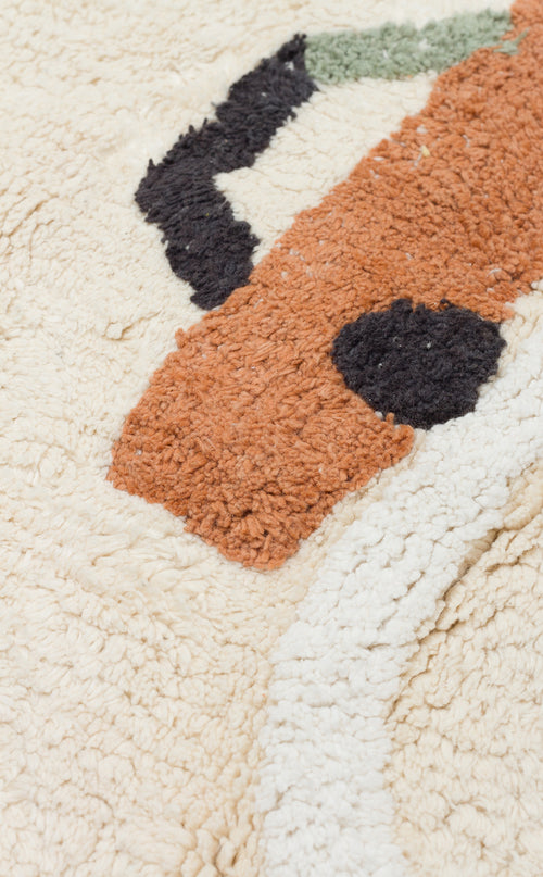 Load image 1 in gallery view. Close-up of the Tiny Voyage - Washable Shaggy - CBN09 rug: a cream cotton playroom rug with a soft, textured surface featuring abstract orange, black, and green patterns.