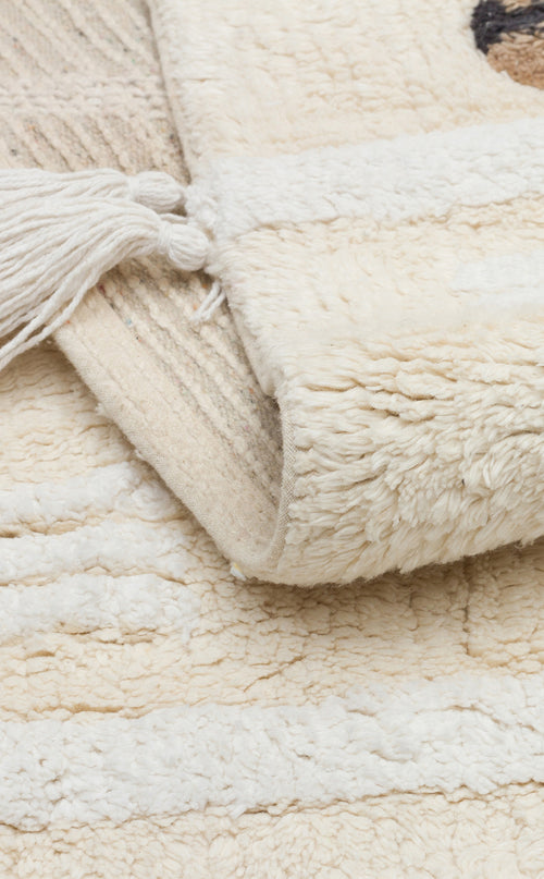 Load image 1 in gallery view. Close-up of the Tiny Voyage - Washable Shaggy - CBN09 cream cotton playroom rug, featuring thick, soft fibers and tassels on one edge, shown atop a similarly textured surface.