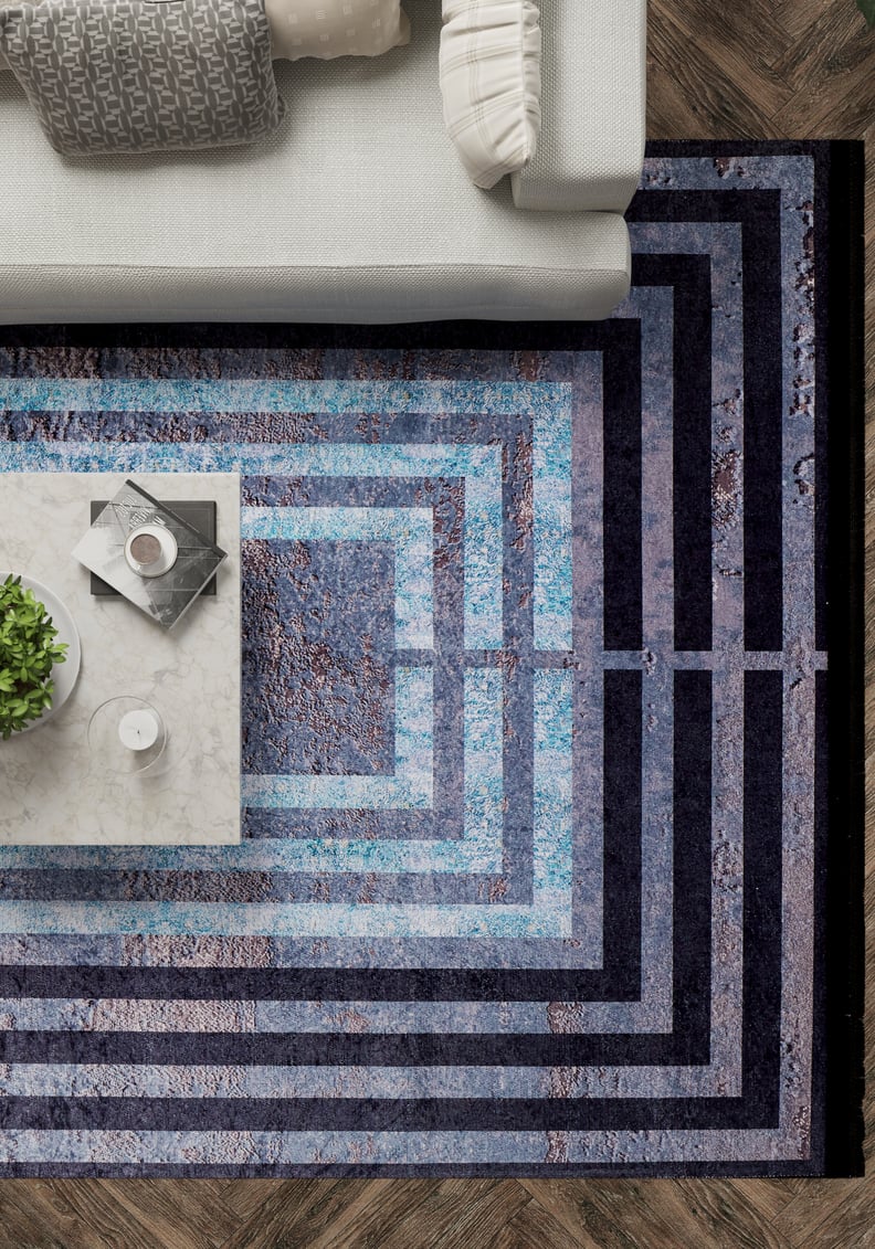A top-down view of a living room with a gray sofa, marble coffee table with a plant and drinks, and the Traditional and Timeless - Washable Rug - JR1408 (Custom Size) in black and blue on dark wood flooring—ideal for high-traffic areas.