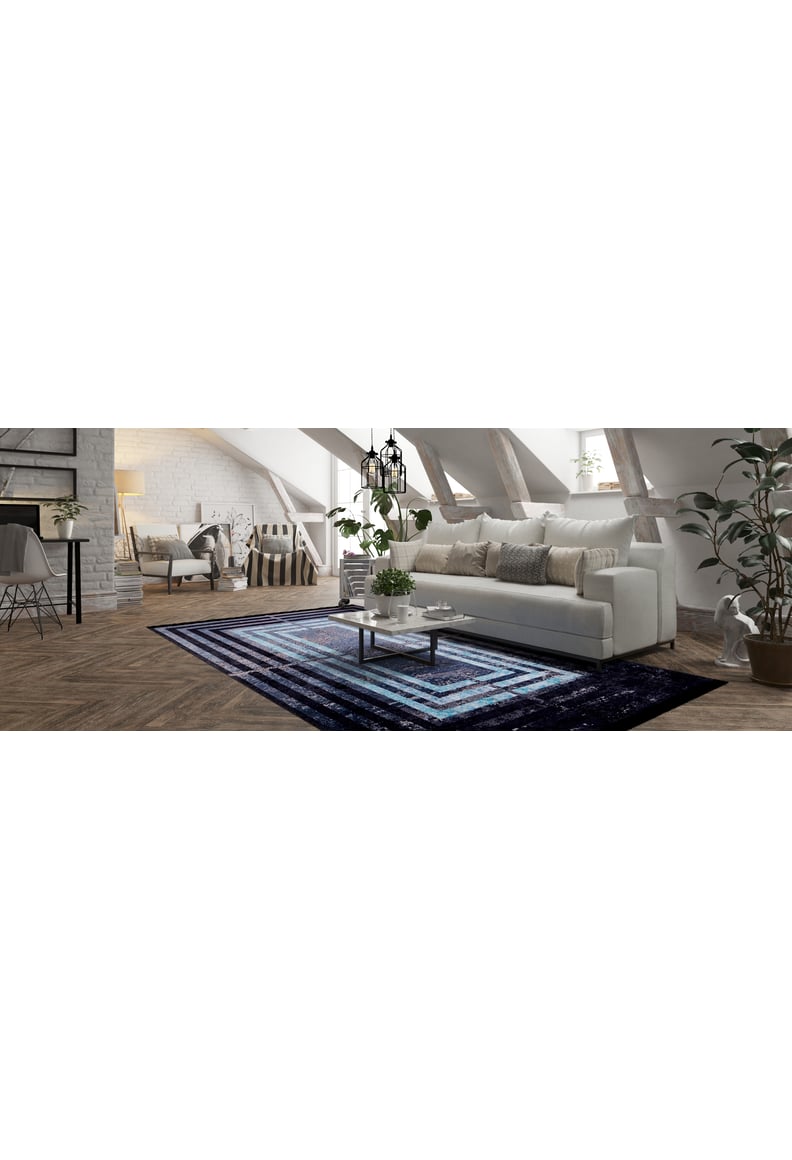 A modern loft living room features white walls, slanted ceilings, a white sofa, coffee table, and the Traditional and Timeless - Washable Rug - JR1408 (Custom Size) in black and blue—perfect for high-traffic spaces.