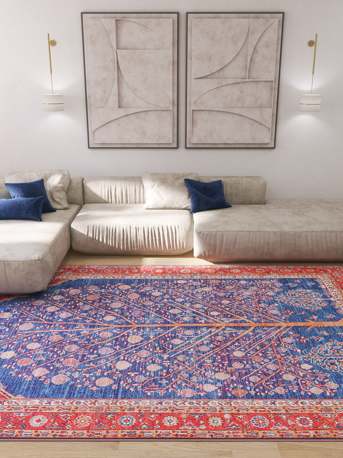 A modern living room with cream sectional sofas, blue pillows, abstract wall art, gold sconces, and the Tree of Plenty Red Blue Washable Rug (LCC3031)—its vibrant blue and red patterns are ideal for high-traffic wooden floors.