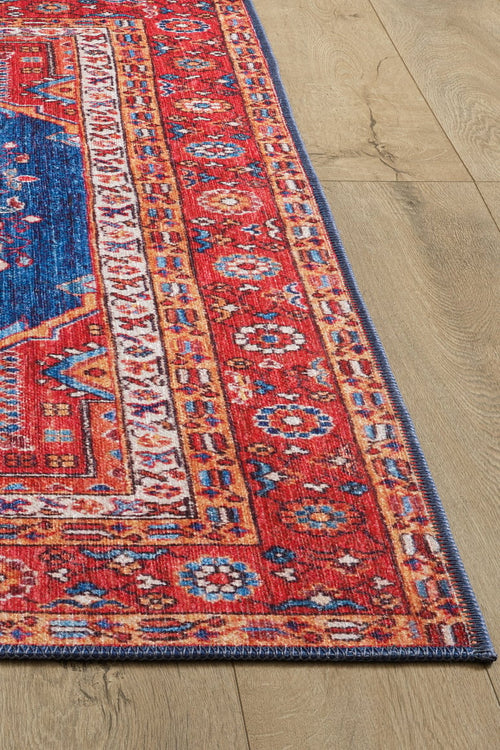 Load image 1 in gallery view. A corner of the Tree of Plenty Red Blue Washable Rug - LCC3031, featuring vibrant geometric and floral patterns, lies on a light wood floor—perfect for high-traffic areas.