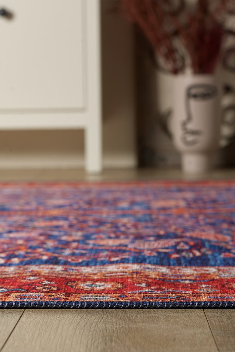 A close-up of the Tree of Plenty Red Blue Washable Rug (LCC3031) on a wooden floor, with a white cabinet and a face-design vase in the blurred background—ideal for high-traffic areas.