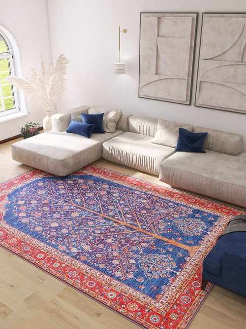 Bild 1 in Galerieansicht laden. A modern living room with a large beige sectional, blue accent pillows, abstract wall art, potted pampas grass, and the Tree of Plenty Red Blue Washable Rug (LCC3031)—ideal for allergy-sensitive or busy areas—showcasing a vibrant tree pattern on the wooden floor.