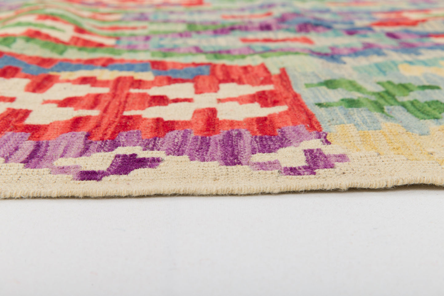 Close-up of the edge of Tribal Essence - Handwoven Kilim, featuring vibrant geometric patterns in red, white, purple, green, and blue. The flatweave texture and intricate craftsmanship are clearly visible against a white background.