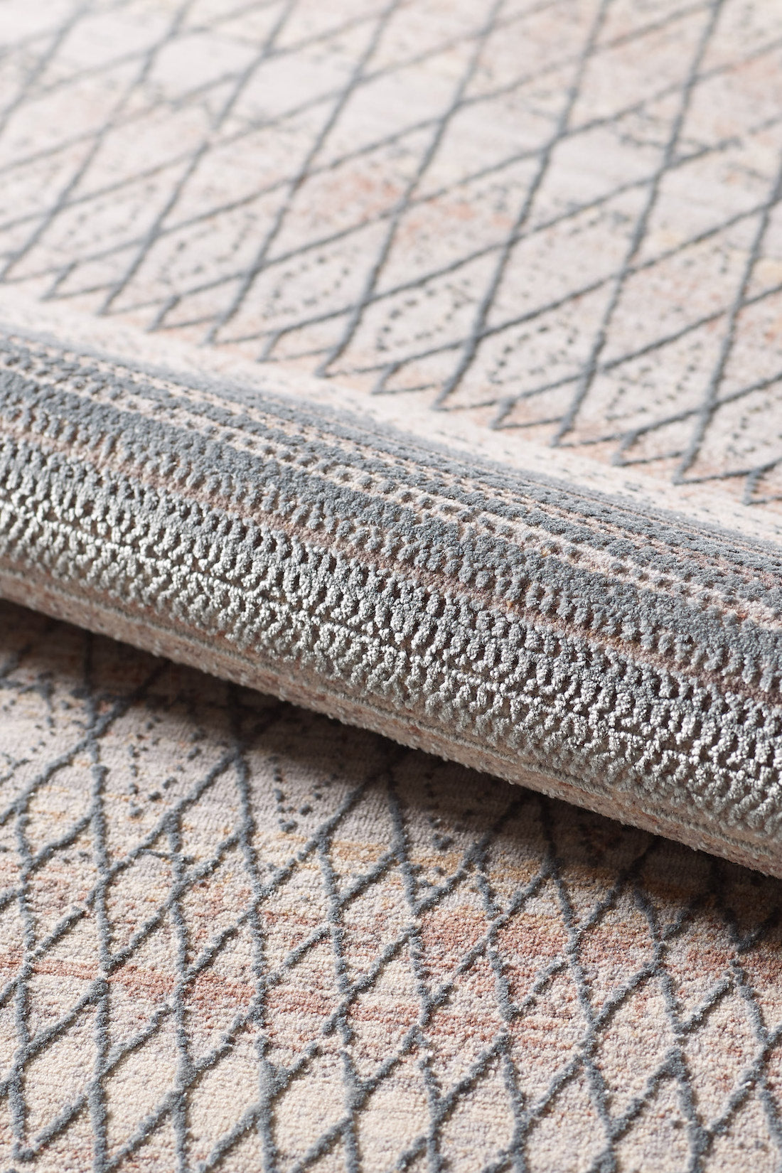 A close-up of the Tribal Essence Trellis Rug - HRD005, rolled to showcase its geometric diamond pattern in beige, gray, and light peach tones with a textured surface.