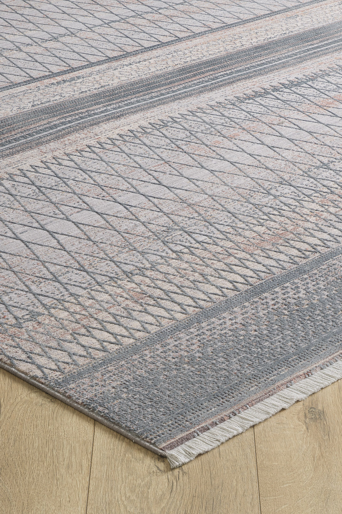 A close-up of the Tribal Essence Trellis Rug - HRD005 shows its modern geometric patterns in gray and beige on a wooden floor. This machine-made rug features edge tassels for added texture.