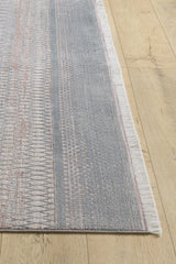 A corner of the Tribal Essence Trellis Rug - HRD005 features gray and light pink patterns with white fringed edges, displayed on a light wooden floor.