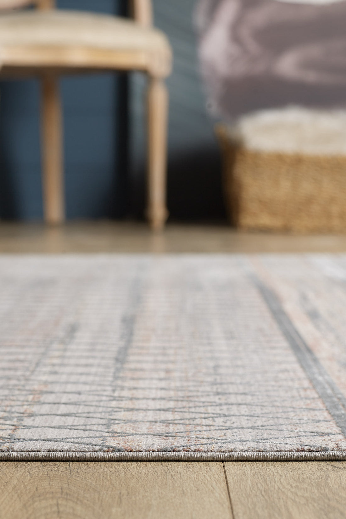 A close-up of the Tribal Essence Trellis Rug - HRD005 on a wooden floor, with part of a woven basket and a wooden chair softly blurred in the background.