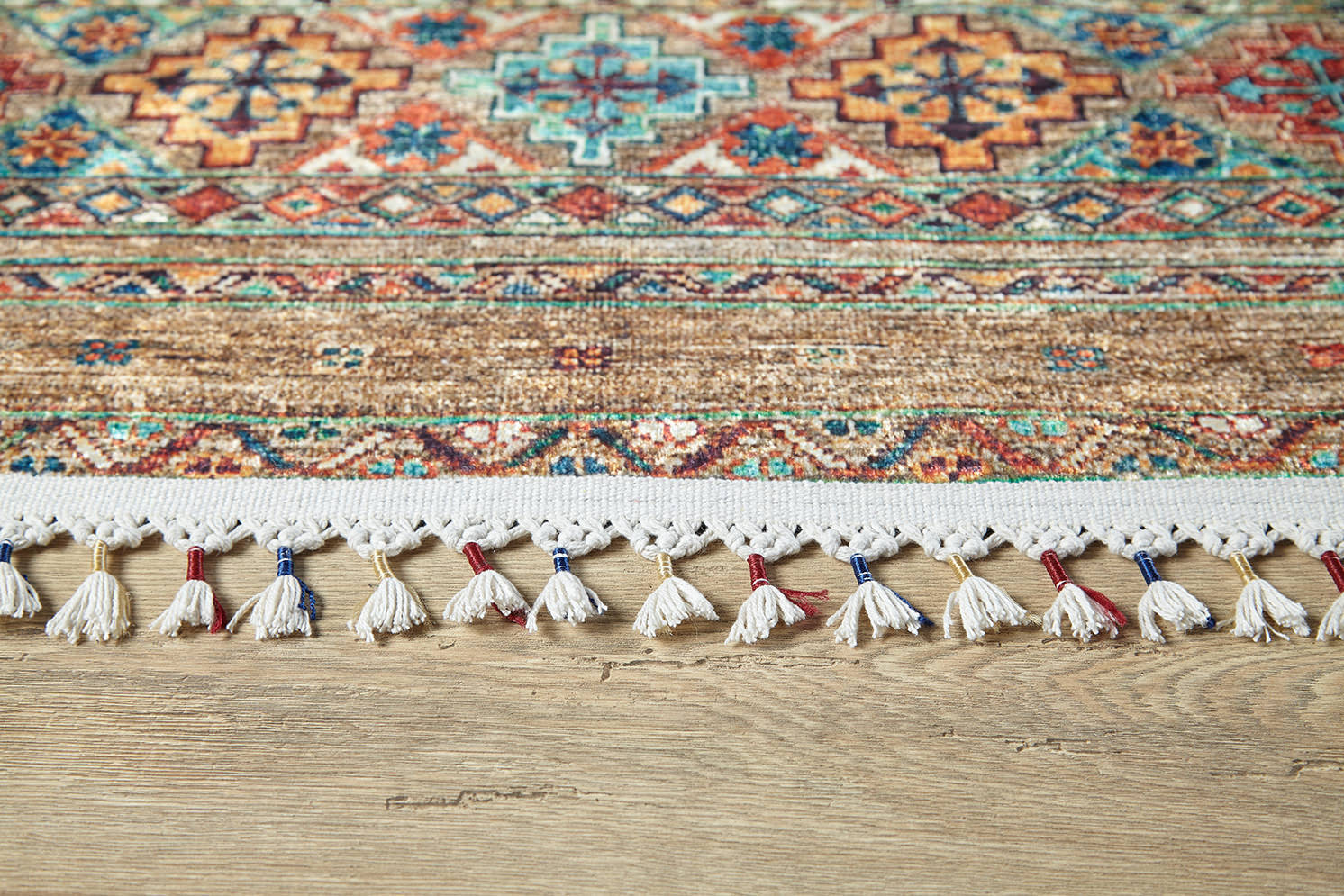 A close-up of the Tribal Tango - Washable Rug - JR5089 (Custom Size), featuring colorful geometric patterns in red, blue, and orange with a white tasseled fringe—ideal for high-traffic areas—shown on a light wooden floor.